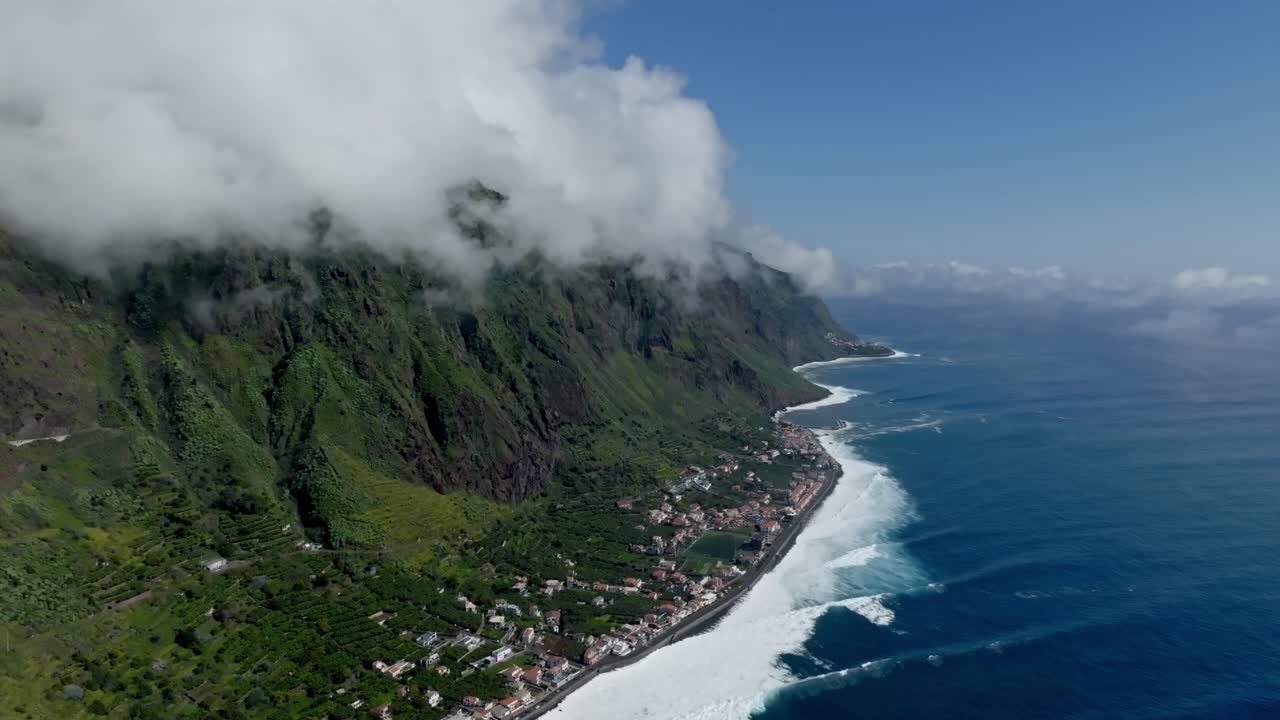 Waves crash onto shore while clouds roll down the mountain at Faj&atilde; da Ovelha