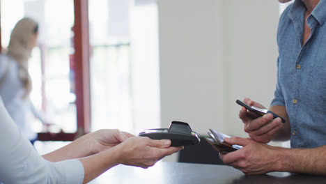 hombre caucásico hablando y pagando con teléfono inteligente en la recepción de una clínica dental moderna