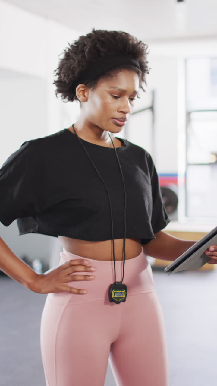 Vertical video portrait of smiling african american female fitness trainer at a gym with tablet