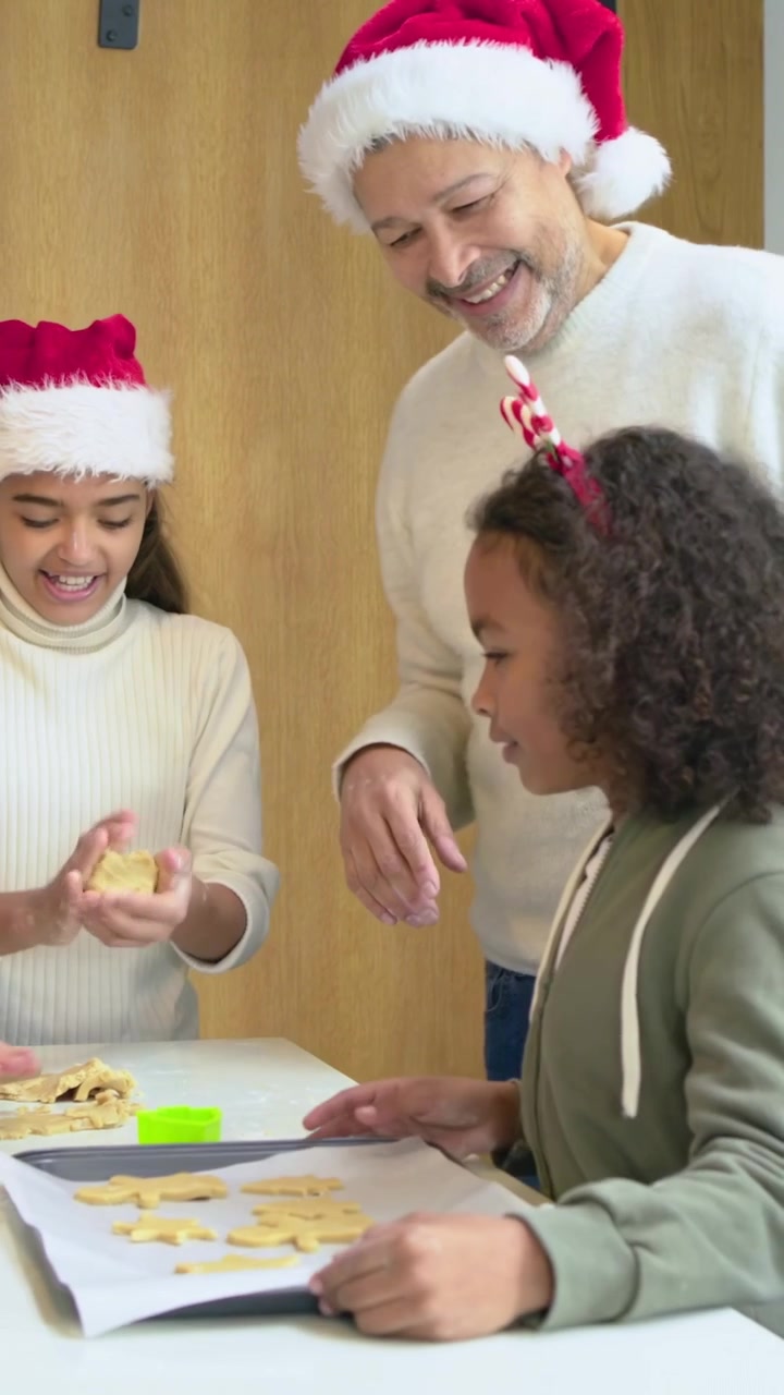 Video verticale: Donna sorridente con corna che guida i bambini a tagliare l'impasto per i biscotti in cucina.