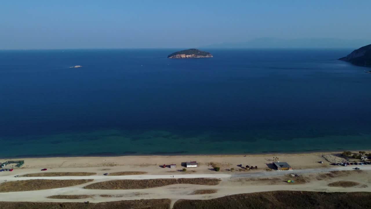 멀리 작은 그리스 섬이 있는 해변 위의 느린 공중 팬