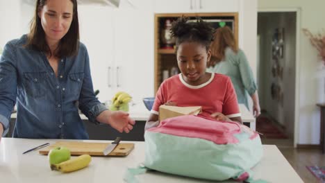 feliz mujer caucásica y su hija afroamericana empacando comida juntos