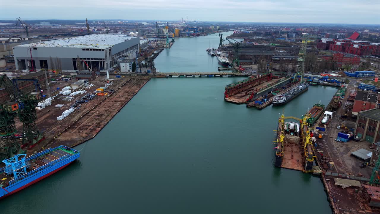 Establishing aerial overview of Gdansk Shipyard with cranes, Martwa Wisla river, and cityscape, boats in dry barges