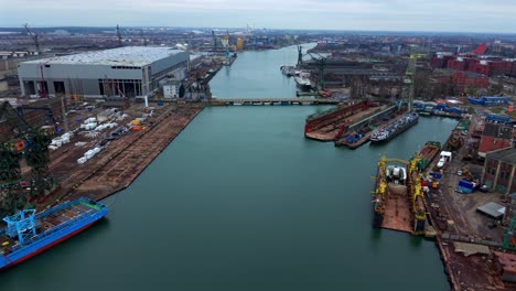 establishing aerial overview of gdansk shipyard with cranes, martwa wisla river, and cityscape, boats in dry barges