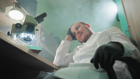 a close-up view of a scientist in a white lab coat, sitting and resting with eyes closed, hand on forehead, in a laboratory setting