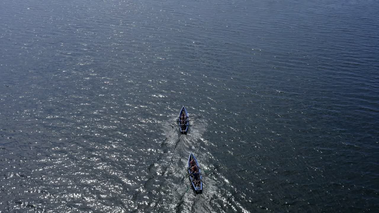 Drone top down view tracking behind currach boats rowing in open ocean