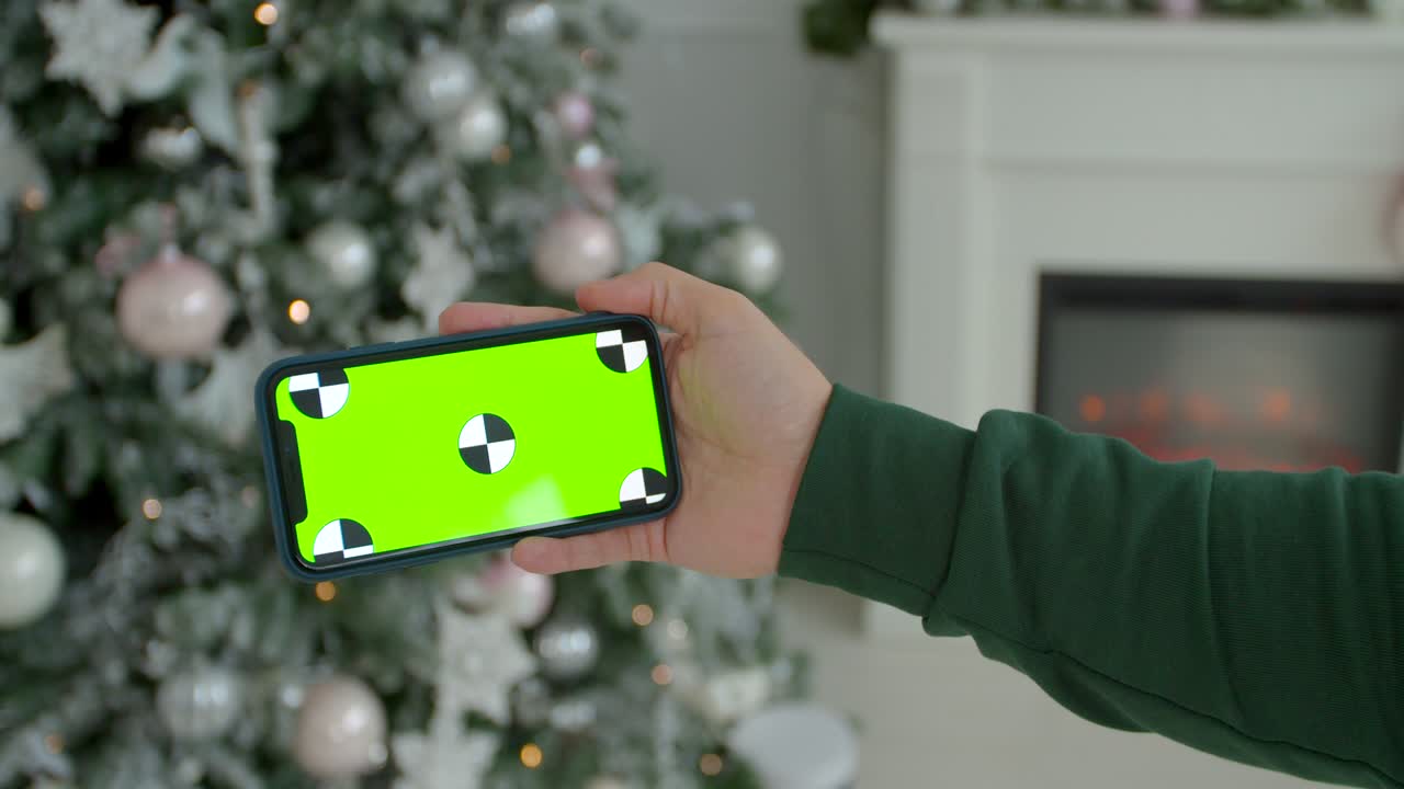 hombre sosteniendo una maqueta de teléfono inteligente pantalla verde llave de cromo en la habitación decorada para el año nuevo. primer plano de manos masculinas sosteniendo un teléfono inteligente moderno negro en las manos en el interior de la casa de navidad brillante.