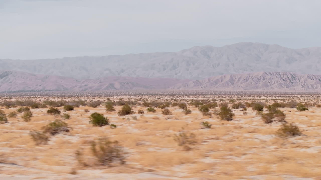 Experience a breathtaking aerial journey over a sprawling desert, showcasing endless sandy plains and distant mountains under a clear sky. The tranquil mood evokes a sense of isolation and beauty