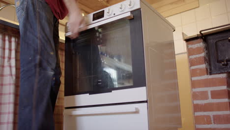 man slides out and removes broken white oven from its spot in kitchen, low angle