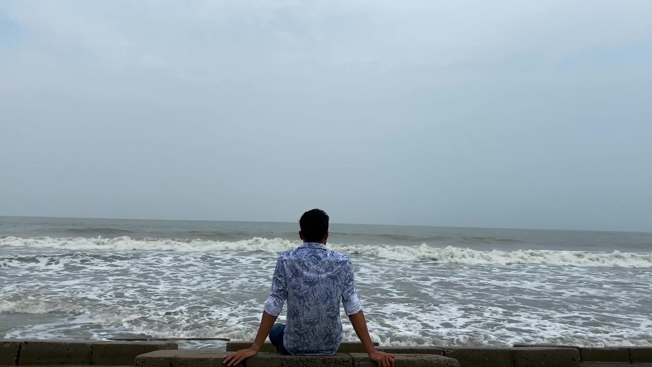 Uomo solitario seduto su una vasta riva del mare che osserva le onde dell'oceano con il cielo - inquadratura statica