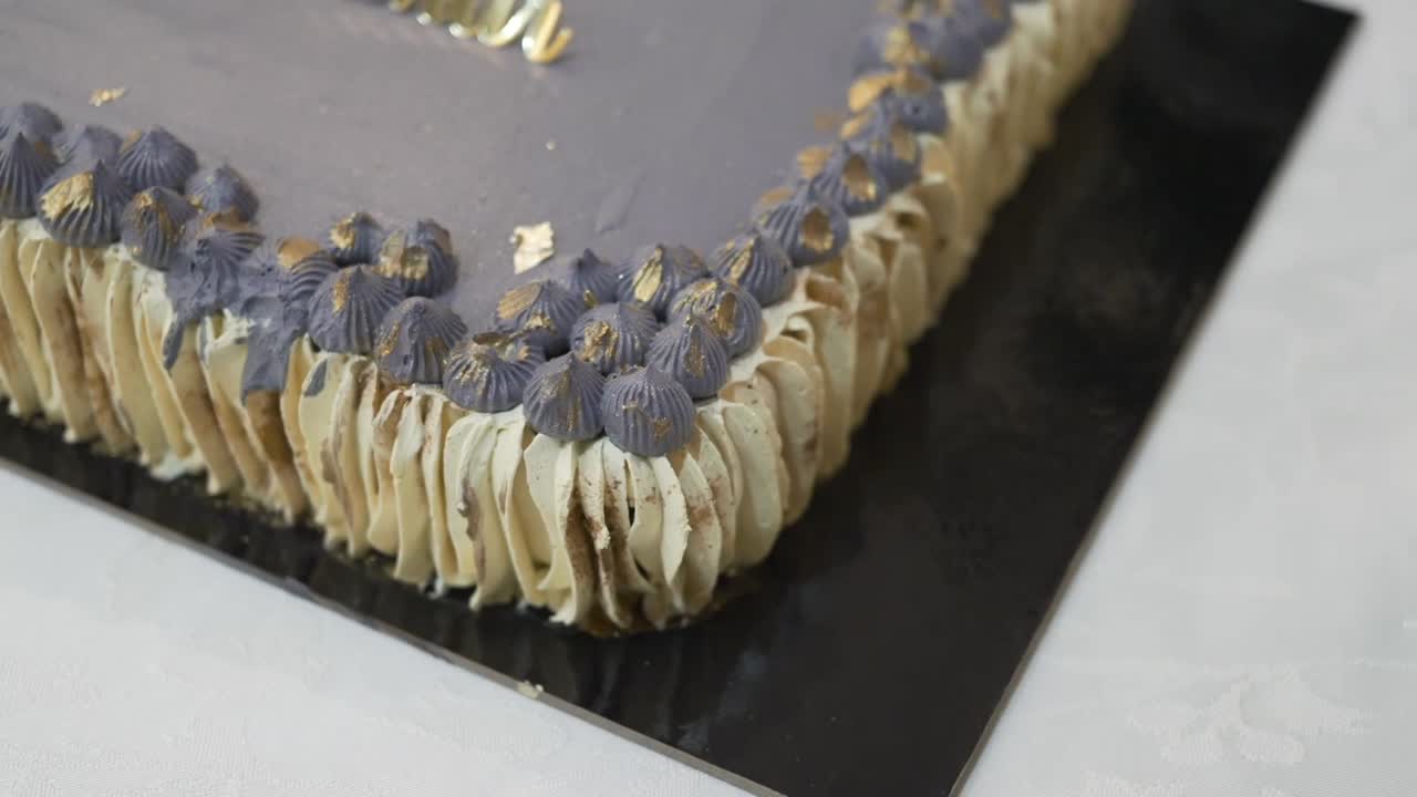 Close up of a cake with gold accents and lavender buttercream details on a black base