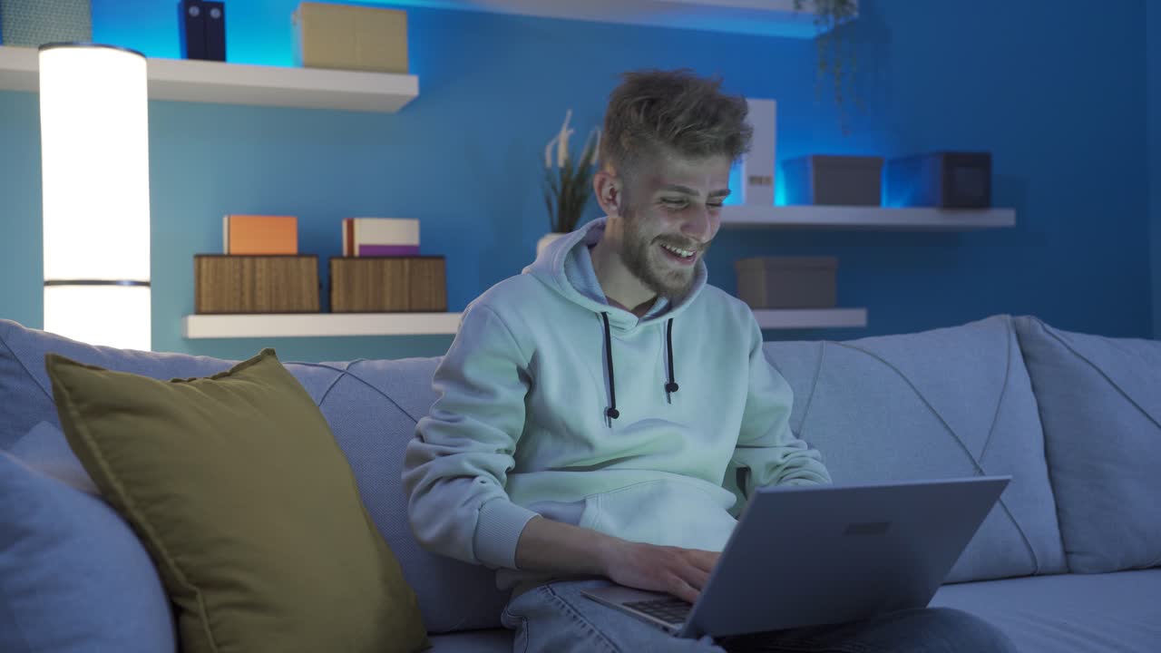 joven feliz bailando en casa divirtiéndose usando una computadora portátil.