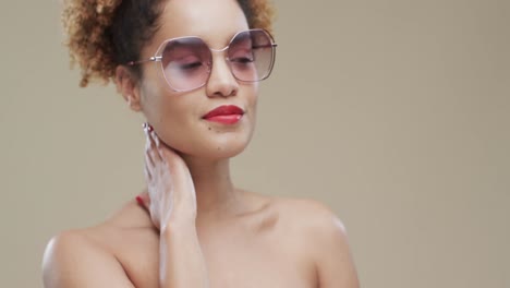 Biracial-woman-with-dark-hair-wearing-sunglasses-on-beige-background-with-copy-space,-slow-motion