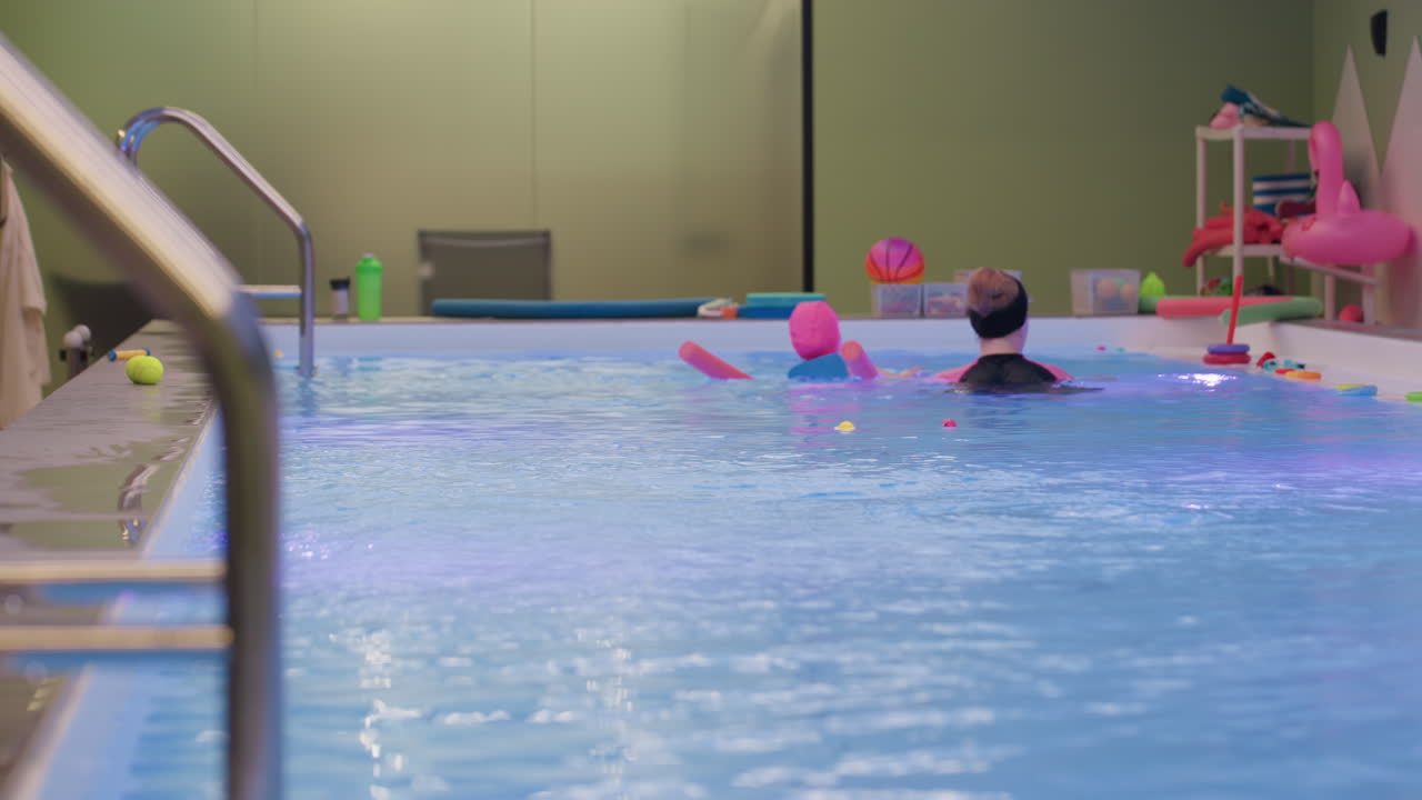 Baby girl diving freely under bright pool light, smooth turns, tiny bubbles rising, confident kicks, gentle supervision nearby, fun summer swim practice, joyful motion captured from side view