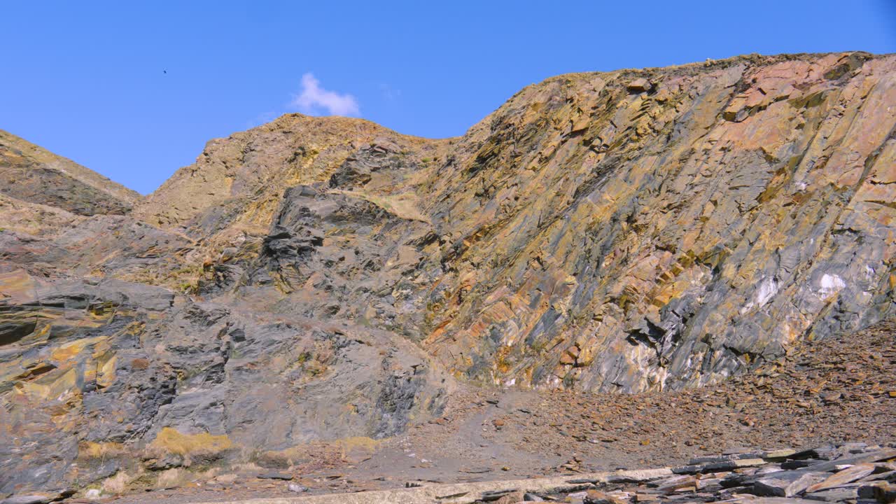 Steep Cliffs in Old Abandoned Slate Quarry as Camera Pans Down with Blue Sky Background.