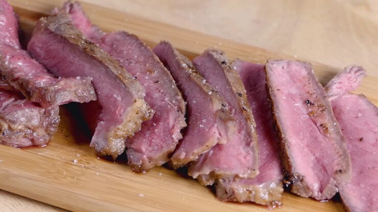 Rekaman slider gerak lambat saat membumbui steak setengah matang di atas talenan saji kayu.