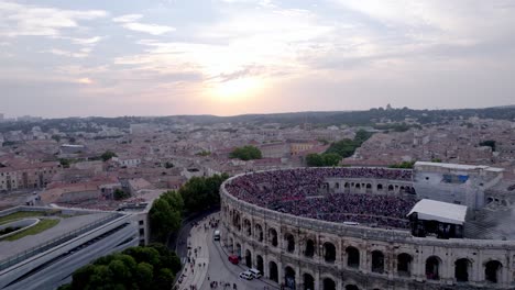 Drone-over-the-Arena-of-Nimes-at-sunset-and-city,-people-are-waiting-for-the-stromae-concert