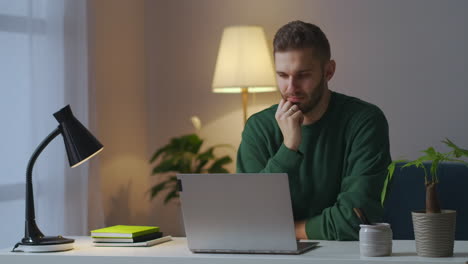 adult man is viewing video or cinema on display of notebook at home at evening learning and entertainment sitting at table