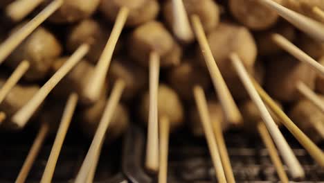 close-up, panning shot of grilled meatball on skewers stacked on hot charcoal grill at street food stall