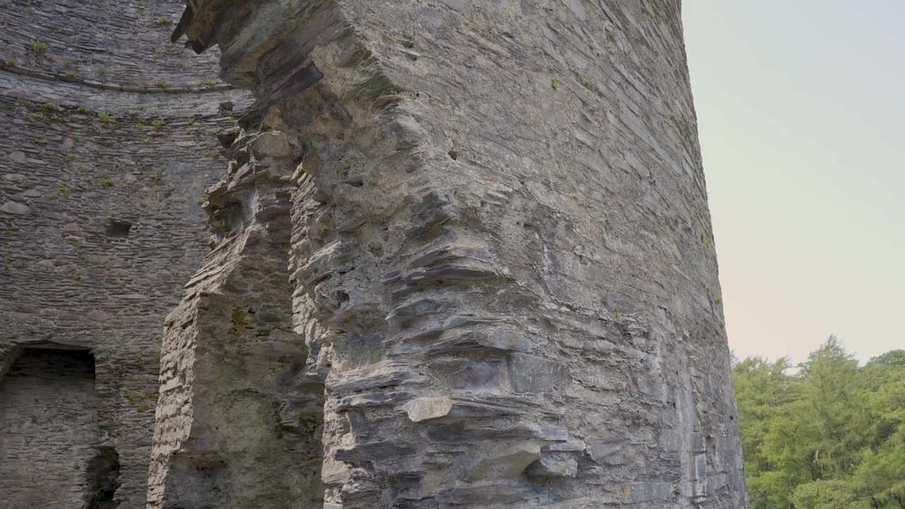 Vista detalhada do exterior da torre do castelo de Dolbadarn, com a câmera movendo-se para cima, exibindo os detalhes da alvenaria das ruínas da torre arredondada e do arco da porta. 4k 30fps