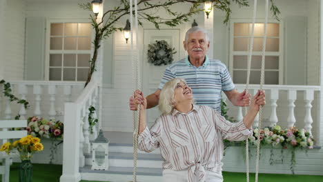 senior couple together in front yard at home. man swinging woman. happy mature retired family