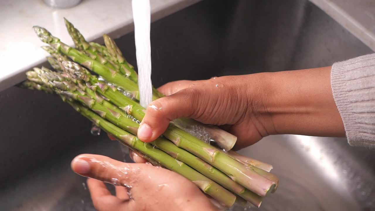 Mani che lavano asparagi verdi freschi sotto acqua corrente in un lavello da cucina