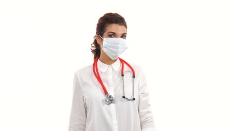 female doctor looking in camera and taking on a operation protection mask. close up of a female surgeon with stethoscope and lab coat isolated on white background dressing up surgical mask