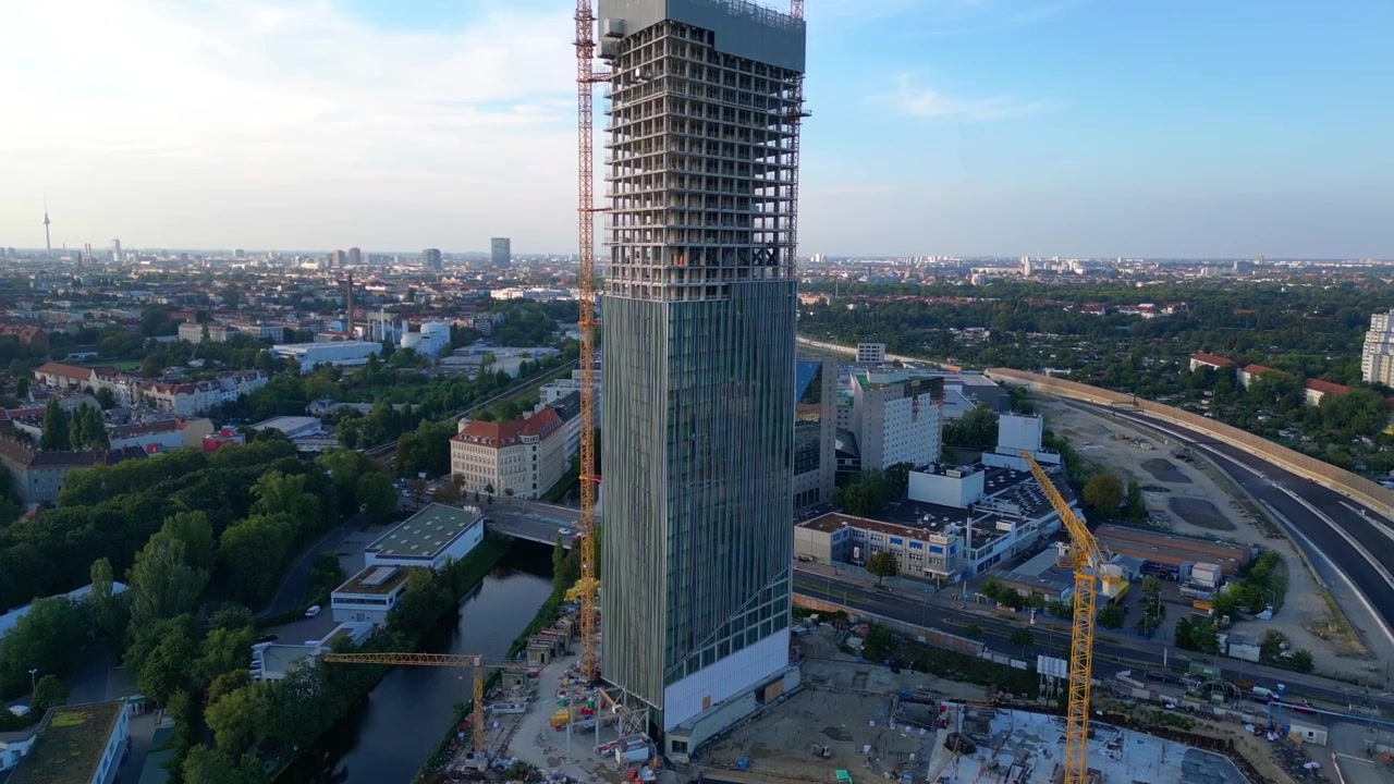Строительная площадка башни Estrel в Берлине 2024 года, с кранами и городским пейзажем на заднем плане. Потрясающий вид с дрона: полет с подъемом камеры