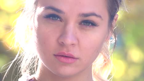 Beautiful-slow-motion-close-up-of-a-confident-young-female-in-bright-sunshine-in-the-park-looking-confidently-into-the-camera