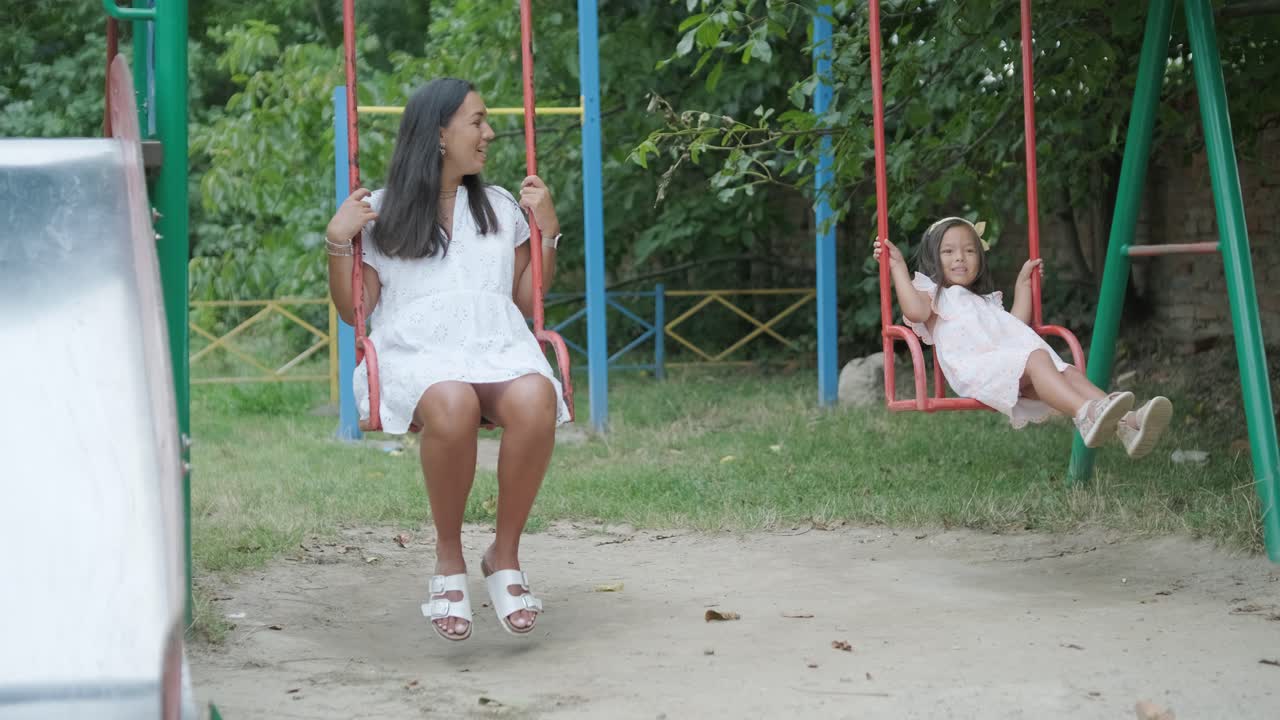 una madre embarazada y su hija joven disfrutan de un tiempo de juego juntos en un patio de recreo en el parque, rodeados de árboles y vegetación