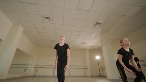 un grupo de jóvenes estudiantes de ballet con ropa de baile negra practicando posiciones en un amplio estudio de ballet con pisos de madera y barras montadas en la pared. expresiones enfocadas y movimientos sincronizados.