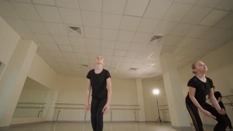 a group of young ballet students in black dancewear practicing positions in a spacious ballet studio with wooden flooring and wall-mounted barres. focused expressions and synchronized movements.