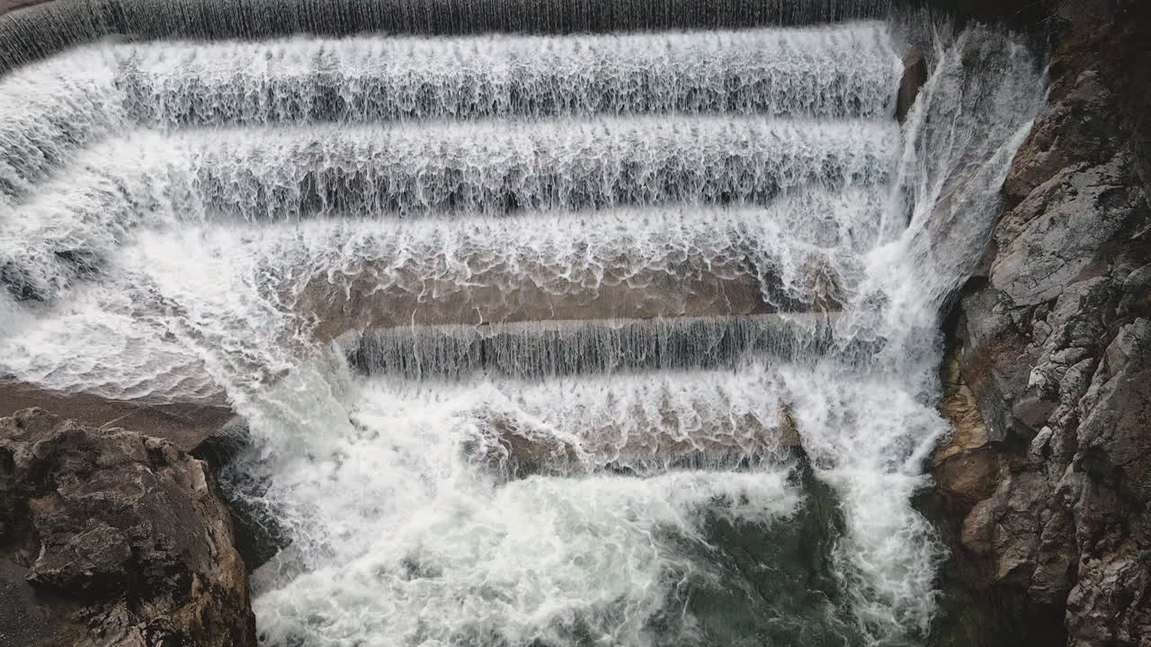 Slow motion drone pans up Lechfall's dramatic tiered dam in Fussen, emphasizing roaring multi-level cascade, foam and rocky drop into turquoise gorge. Hypnotic Bavarian hydro