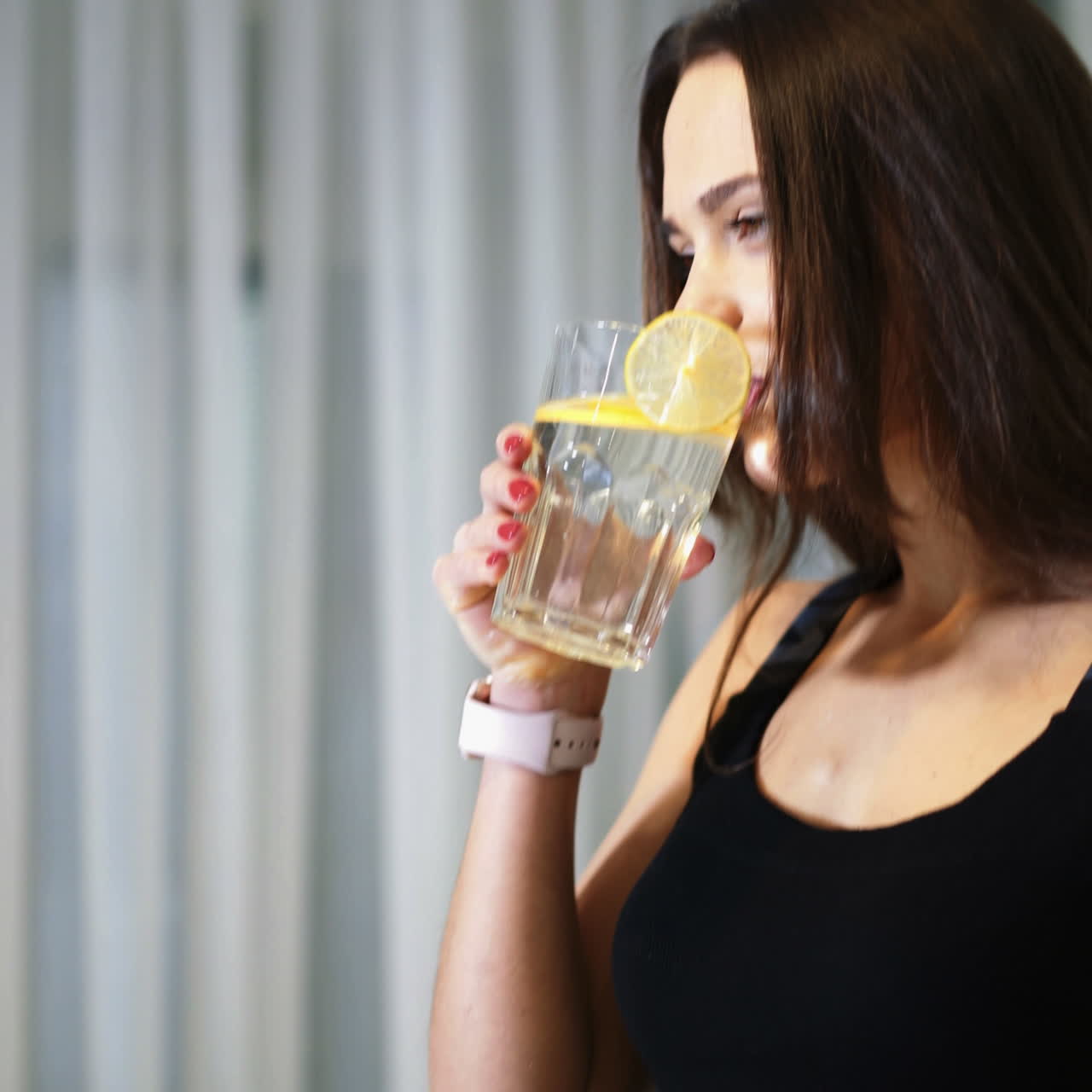 Sportive young woman with a glass of water with a lemon in the kitchen. Healthy lifestyle. Detox-vitaminized water. Concept of diet. Square video