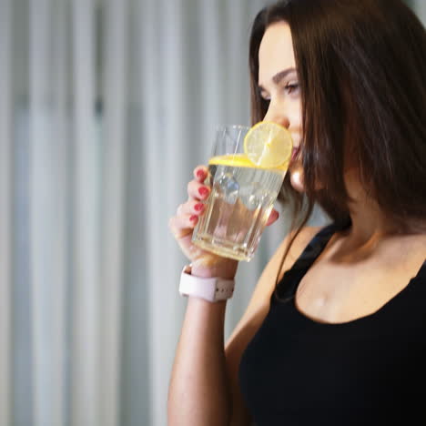 sportive young woman with a glass of water with a lemon in the kitchen. healthy lifestyle. detox-vitaminized water. concept of diet. square video