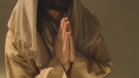 close up shot of man wearing robes with long hair and beard representing figure of jesus christ praying 1