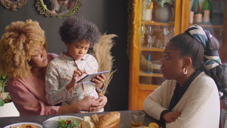 boy sitting with mom and using tablet at family dinner