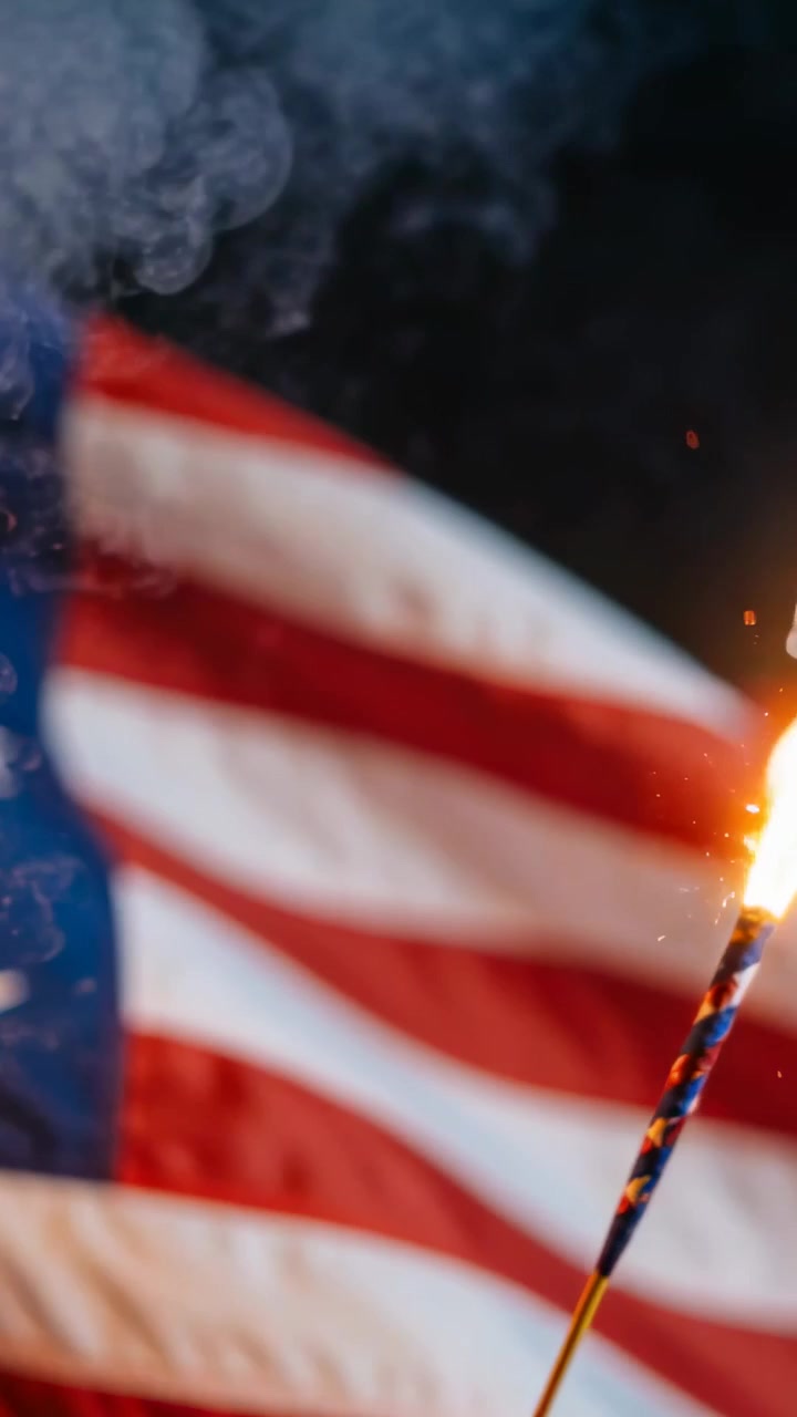 Vertical video: Waving American flag fluttering outdoor at night, sparkler burning, smoke drifting