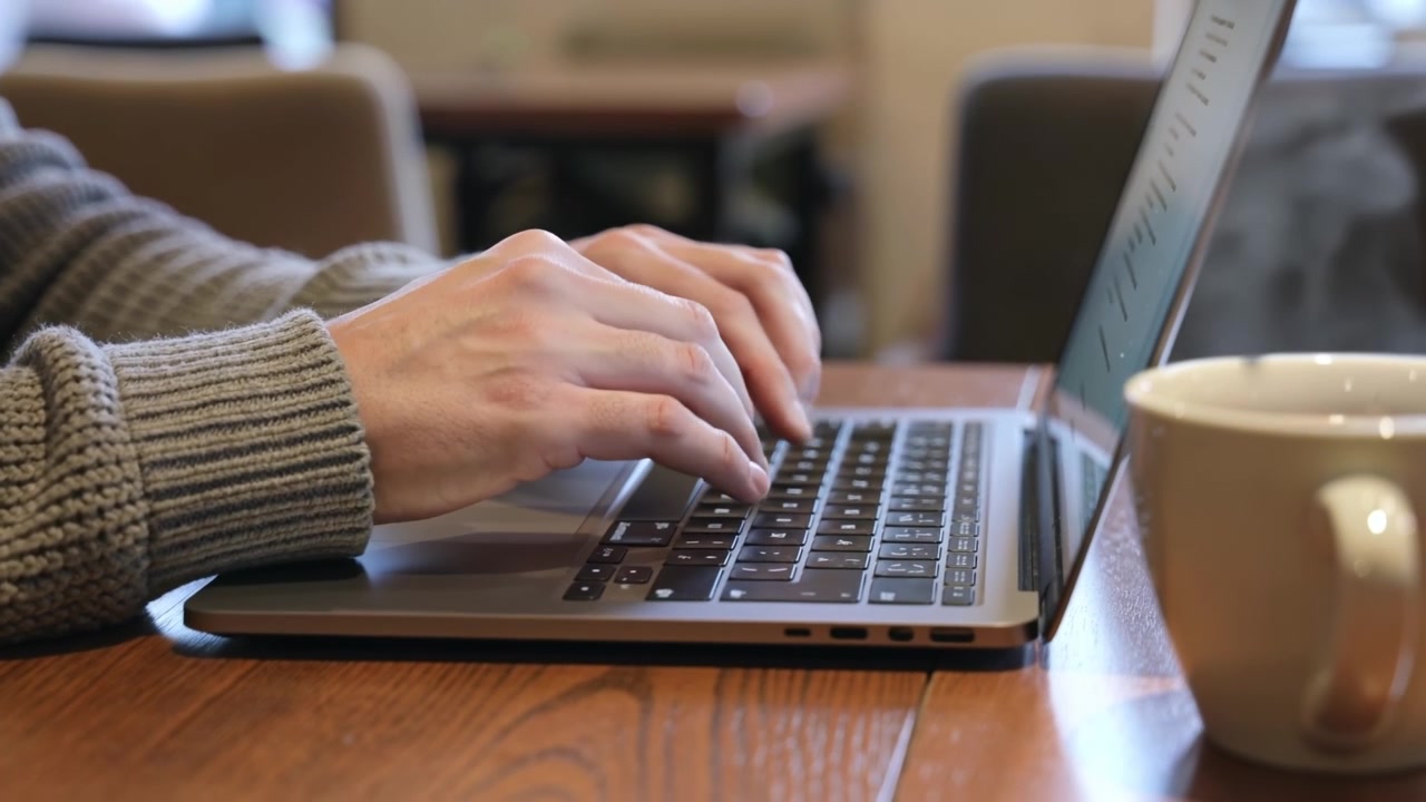 Close up of hands typing on a laptop computer keyboard on a wooden table