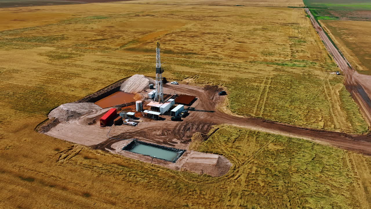 Flight around the small site for natural resources drilling in the vast field. Equipment and cars, two pools are at the location.