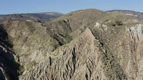 dramatic rock formation on a mountain side with blue sky and green foliage.