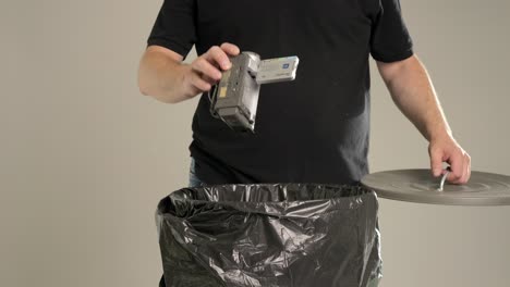 un hombre está tirando una cámara doméstica anticuada muy pequeña en el cubo de la basura