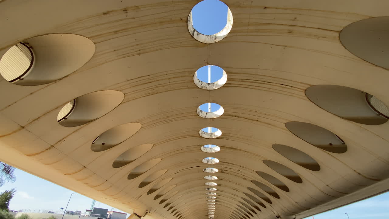 Vista astratta dal basso verso l'alto di aperture circolari in un soffitto di cemento consumato a Siviglia, cielo blu incorniciato da motivi geometrici. Prospettiva suggestiva sotto una moderna struttura in cemento a Siviglia