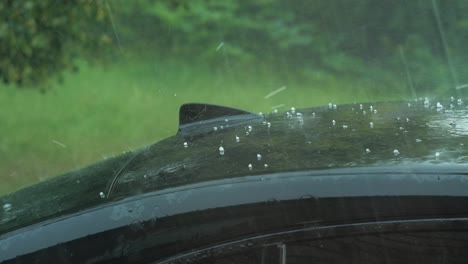 View-of-heavy-storm-hail-and-rain-falling-on-a-black-car,-nature-disaster,-climate-changes,-global-warming,-hot-summer-day,-medium-closeup-shot