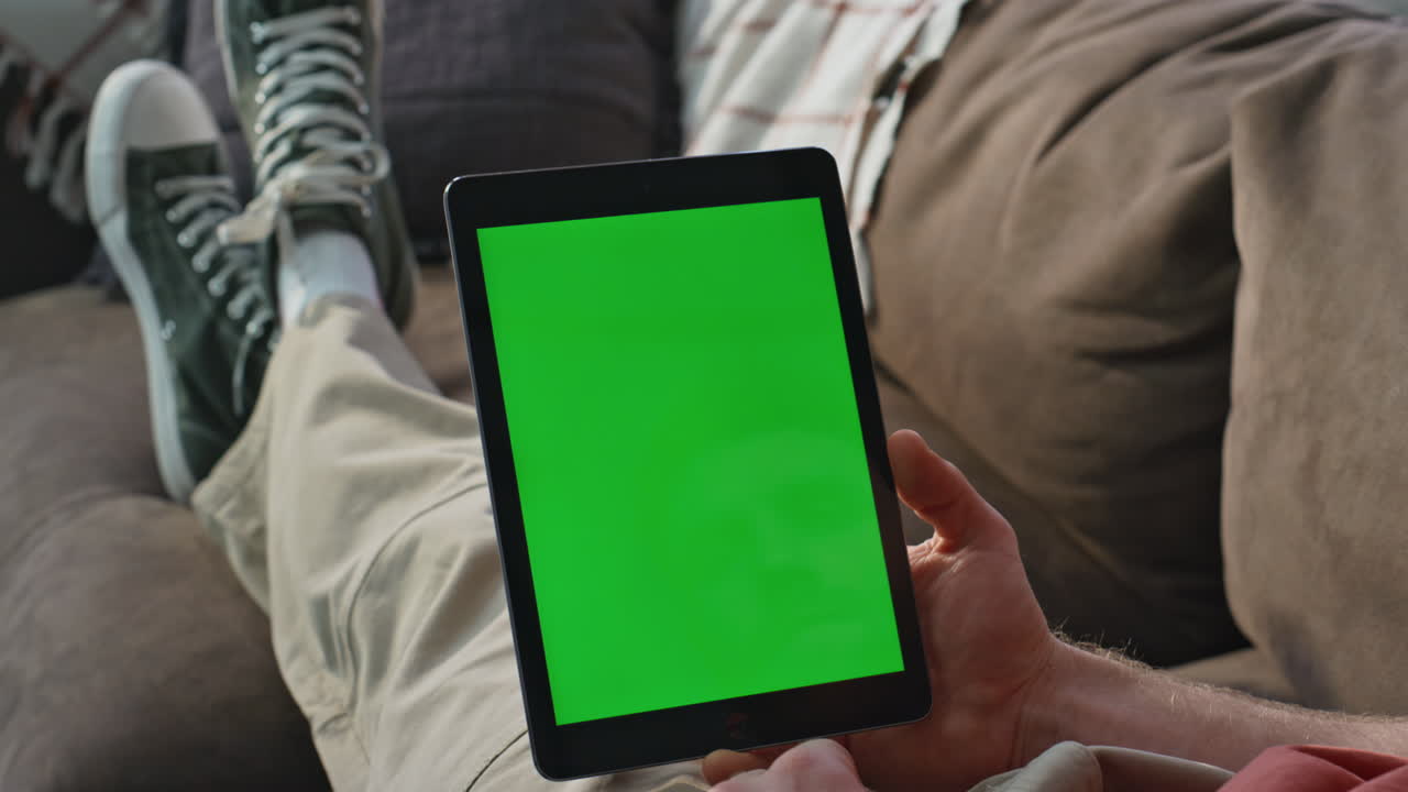 Student watching greenscreen tablet webinar on couch closeup. Man browsing home