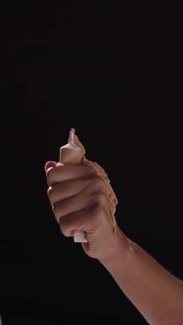 close up of woman squeezing tube of make up until contents squirt out shot on black background