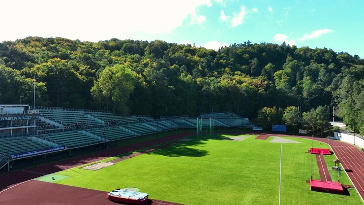 Cinematic aerial shot of a professional running track and sports stadium nestled in a dense green forest. Ideal for wellness, fitness, and sustainability themes.