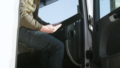 worker wearing vest and cap organizing a truck fleet in a logistics park while reading documents in a truck