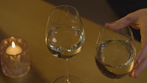 close up of man picking up two glasses of wine on romantic evening at home in lounge with candles