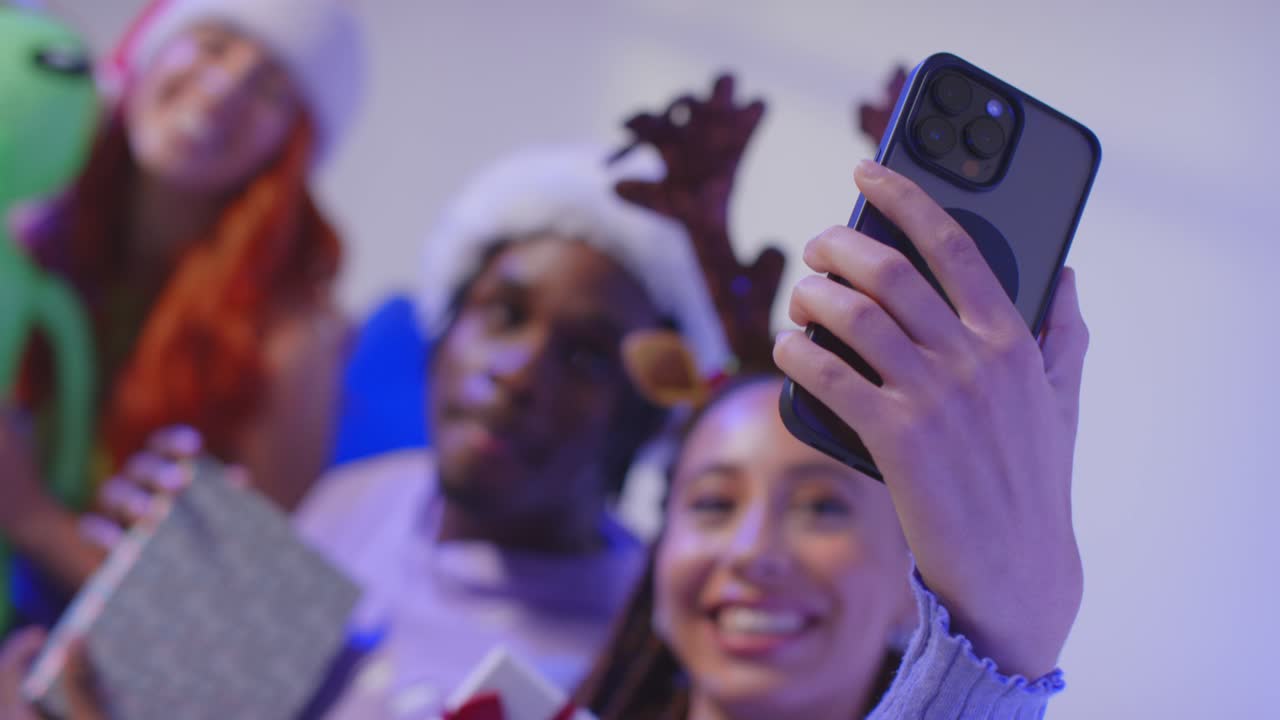 fotografía de estudio de amigos de la generación z en navidad sentados en el sofá con sombrero de papá noel y cuernos de renos tomando selfies en el teléfono móvil 2